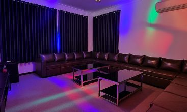 Exterior view of a spacious luxury 7-bedroom villa in Thao Dien, Ho Chi Minh City, featuring a large semi-indoor swimming pool, an elegant living room, a vibrant karaoke lounge with colorful lights, a comfortable king-size bedroom, and modern bathrooms (5 indoor, 3 outdoor).