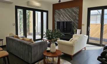 Exterior and interior views of a modern luxury 5-bedroom villa for rent in Thao Dien, Ho Chi Minh City, featuring a unique indoor swimming pool with wooden deck, a stylish living room, a dedicated karaoke room, a king-size bedroom, and 6 contemporary bathrooms (4 indoor, 2 outdoor).